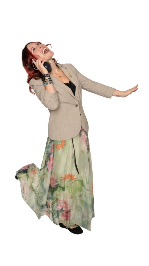 Krystal Lee Moore laughing on a phone call in a blazer and floral skirt