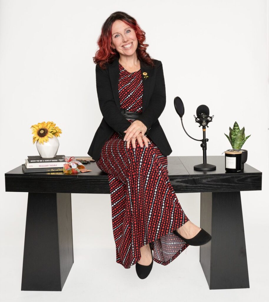 Krystal Lee Moore seated at a podcast desk with a microphone, books and a sunflower